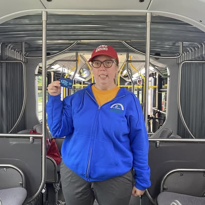 a white woman wearing a blue shirt is standing on a bus holding a bus pass