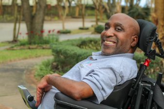 a Black man in a wheelchair wearing a blue polo shirt, smiling at the camera